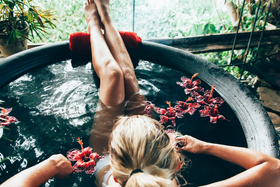 Women bathing outdoors in a round tub with flowers