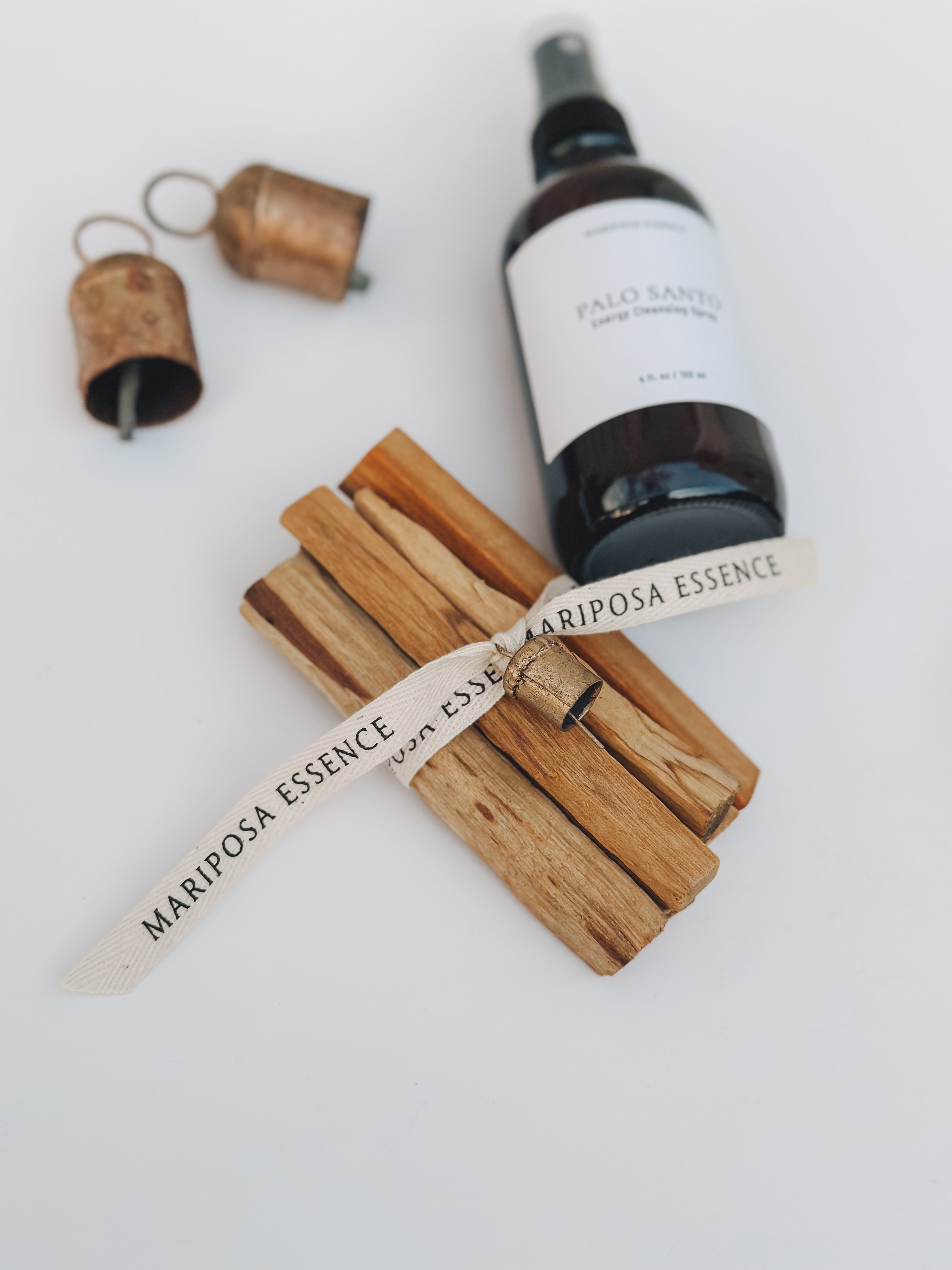 Palo santo sticks bundled and wrapped with cotton ribbon and mini nana bell displayed with Palo santo spray.