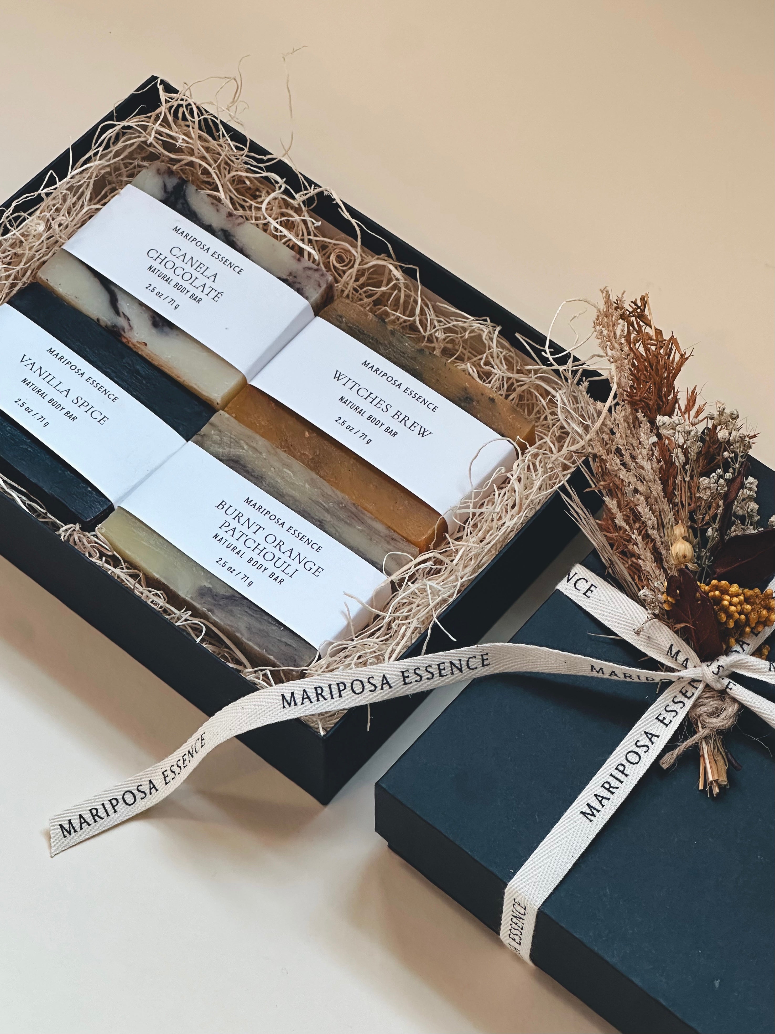 Sample soaps in a black box with natural filler wrapped with a natural cotton branded ribbon with a small bunch of dried flowers.